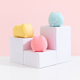 Pusheen Surprise Squishu Assortment including yellow, blue and pink colors on white pedestals. The front and side can be seen of the yellow squishy. The back of the blue squishy can be seen. Lastly, the front of the pink squishy toy can be seen.