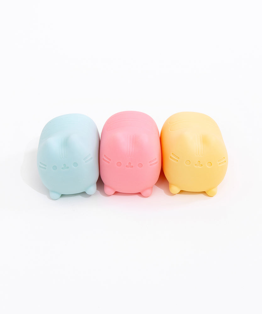 Pusheen Surprise Squishu Assortment of toys. From left to right are blue, pink, and yellow variations of gel-filled toys that resemble Pusheen the Cat.