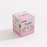 A close-up of the Pusheen Sweets Surprise Plush packaging. The front of the packaging features Pusheen holding a strawberry cake next to another strawberry cake and a cake roll. The side of the box can be seen and it shows the known styles of the blind box series as well as a mystery style.