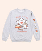 Front and sleeve view of the Pusheen Tea Society Unisex Sweatshirt. The arms are laid out to reveal the printed sleeve detail on the wearer’s left sleeve. The sleeve features rust, cream, and white icons of teacups, biscuits, and a tea kettle. 