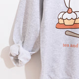 Close-up view of the sleeve and front graphic of the grey unisex sweatshirt. The wearer’s right sleeve is rolled up to reveal the soft interior lining.  