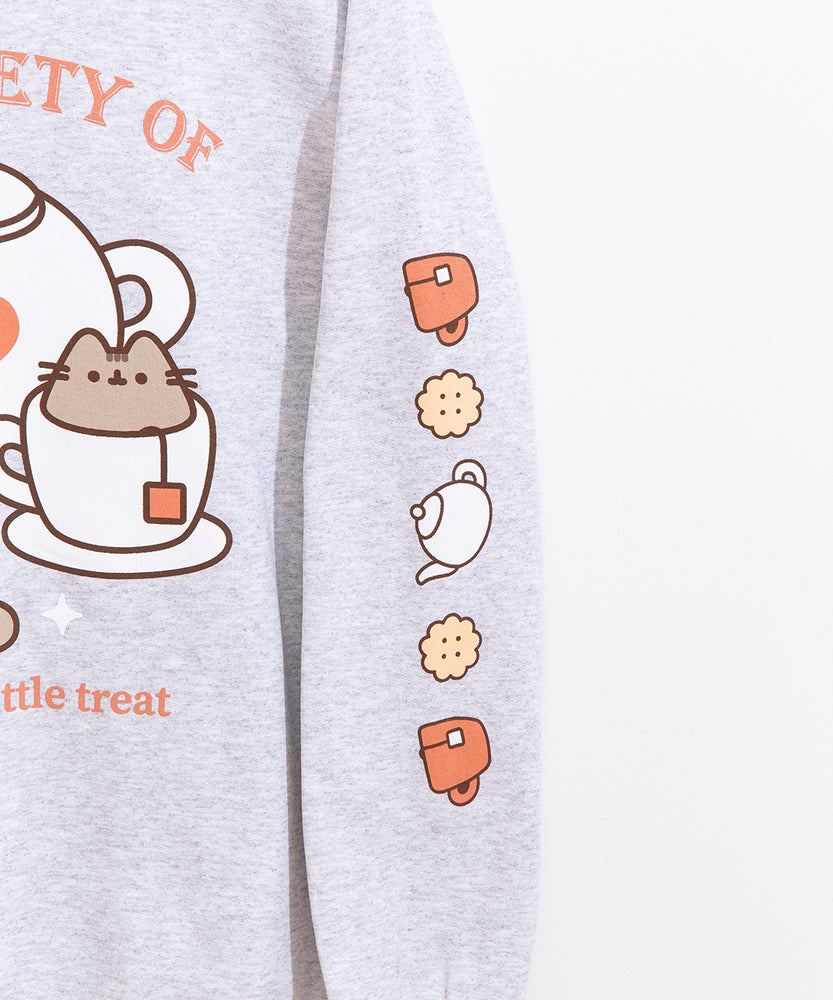 Close-up view of icons printed on the wearer’s left sleeve of the grey sweatshirt. The icons include a salmon teacup, yellow biscuits, and a white tea kettle. 