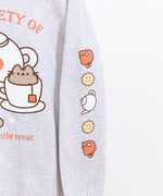 Close-up view of icons printed on the wearer’s left sleeve of the grey sweatshirt. The icons include a salmon teacup, yellow biscuits, and a white tea kettle. 