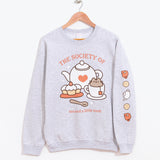Front view of the Tea Society Unisex Sweatshirt. The light grey sweatshirt hangs on a brown wood hanger to show all collar, sleeve, and hem details. 
