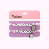 Pusheen & Stormy Best Friends Bracelet Set on its cardboard backing card. The top half of the card has the Pusheen logo in brown on a light pink background and the bottom half of the card is purple. Between the two bracelets is a perforated line to separate the backing card into two pieces. 