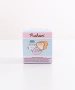 A close-up of the Pusheen’s Kitchen Surprise Plush packaging. The front of the packaging features Pusheen as various kitchen essentials including a white and blue milk jug, cream and light brown white bread slice, and lilac-colored tea pot. The packaging says "Kitchen Surprise Plush.” 