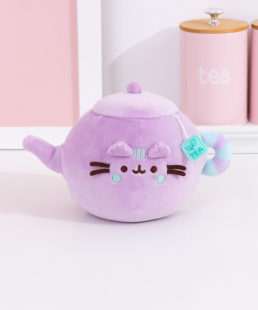 Pusheen's Kitchen Teapot Squisheen Plush sitting on a white surface. Pusheen the Cat takes the form of a lilac tea kettle. One paw extends to become the spout.