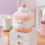 Cake Squisheen shown on a desktop to show scale of 7" tall plush toy. Pusheen the Cat rests inside the cream layer of the cake plush.