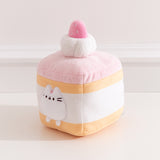 Side quarter view of the strawberry cake Pusheen plush. The cake plush has a light yellow cake layer in the top and at the bottom of the square plush. 