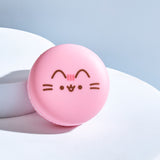 Front view of the Pusheen Strawberry Macaron Lip Balm. The circular component has Pusheen's ears, head stripes, eyes, mouth and whiskers printed in brown and pink on the front.