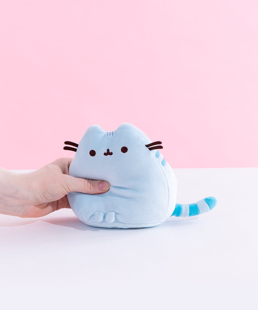 A model’s hand squeezing the Blue Mini Squisheen Plush, demonstrating it’s squishiness.