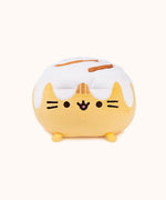 Front view of the Cinnamon Roll Squisheen in front of a white background. Pusheen's frosting covered ears blends in visually with the rest of the frosting on top of her.