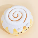 Top view of the Cinnamon Roll Squisheen in front of a cream background. The cinnamon swirl in the frosting is not embroidered, but leaves an indent in the frosting. The swirl starts at the same point as Pusheen's face, and swirls inwards.