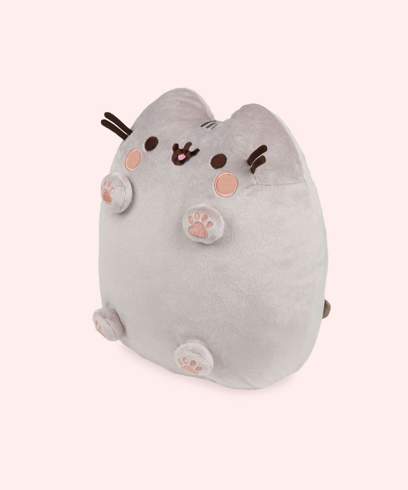 Left quarter view of Pusheen plush. This view shows Pusheen’s four paws extending off her body and to showcase all four bottom of the paws. The plush tail extends slightly off the back of the plush and is peeking out in this angle.