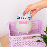 Model holding Pusheen Gaming Lamp to show size of lamp. The grey, light pink, light blue, and orange lamp is held above a purple basket.  