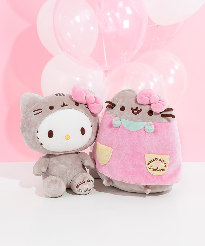 The Hello Kitty and Pusheen collaboration plush sit next to one another in front of a pink background and white and clear balloons.