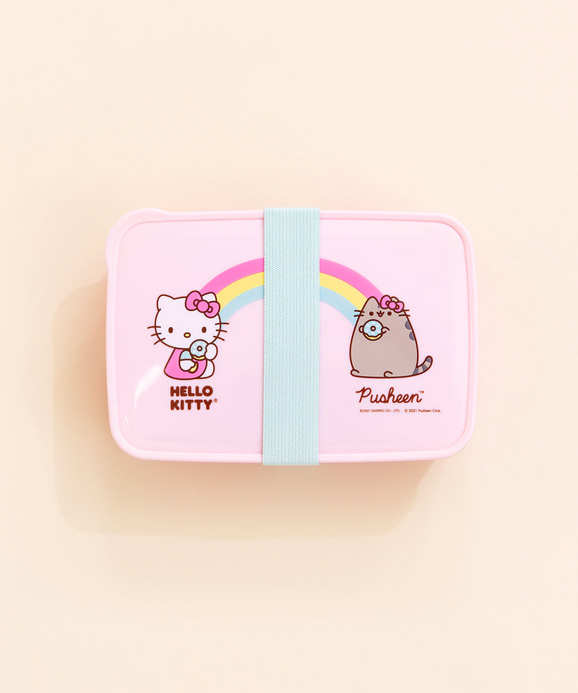 Top view of the Hello Kitty x Pusheen Lunchbox on top of a cream background. The teal rubber band is placed perfectly in the middle, covering the ‘heart’ in the middle. There is a small tab on the upper left corner of the lid.