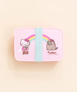 Top view of the Hello Kitty x Pusheen Lunchbox on top of a cream background. The teal rubber band is placed perfectly in the middle, covering the ‘heart’ in the middle. There is a small tab on the upper left corner of the lid.