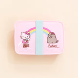 Top view of the Hello Kitty x Pusheen Lunchbox on top of a cream background. The teal rubber band is placed perfectly in the middle, covering the ‘heart’ in the middle. There is a small tab on the upper left corner of the lid.