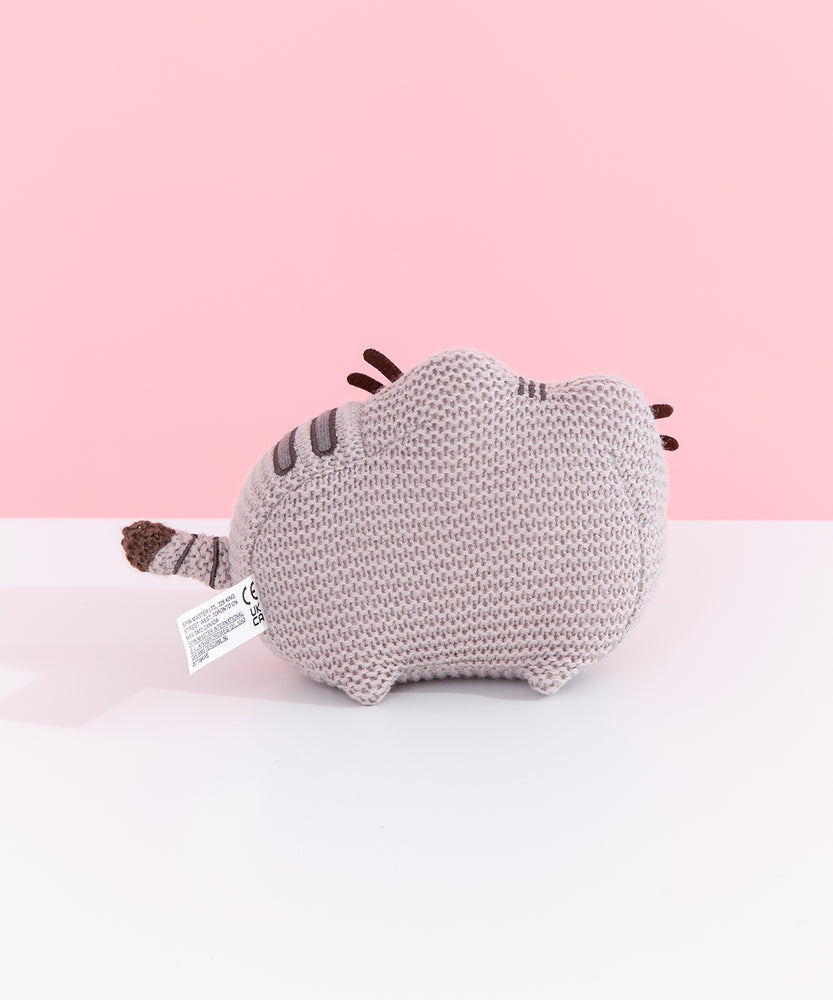 Back view of Knit Pusheen Plush. In this view, the front whiskers can be seen extending off the front of the plush. The plush sits atop little, crocheted paws. 