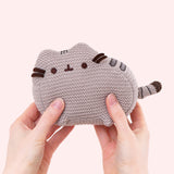 Model holds mini knit plush to demonstrate how small the plush is. Next to model’s right hand, the crocheted grey and brown tail extends off the body of the plush. 