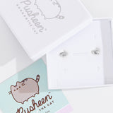 Sterling Silver finish of Pusheen Lazy Stud Earrings in their white packaging box. The earrings are accompanied by the lid of the packaging box and a mint green informational card about the earrings. 