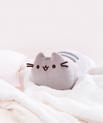 The Medium Log Squisheen buried in a sea of fuzzy white blankets. A light pink pillow on the left is the only life raft in this sea of coziness.