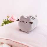 The Mini Log Squisheen rests elegantly on top of a light pink pillow. Pink Peonies and a fuzzy white blanket peek out from the edges of the pillow.