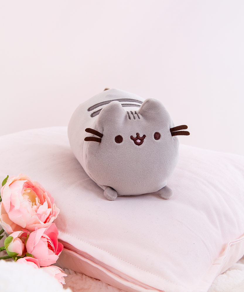 The Mini Log Squisheen takes center stage as she rests elegantly on top of a light pink pillow. Pink Peonies and a fuzzy white blanket peek out from the bottom left.