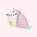 Quarter view of the Magical Lights Mermaid Pusheenicorn Plush facing the left in a light pink space. 