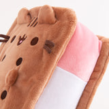 Close-up view of Pusheen Ice Cream Sandwich Squisheen. Pusheen takes the form of an ice cream treat and her classic ears, eyes, stripes, mouth, and whiskers are embroidered at the end of the desert plush. The inside “sandwich” portion is pink, white, and light green. 