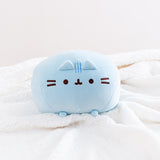 Front view of the Blue Round Squisheen sitting on top a fluffy white blanket. She is angled upwards so her feet emerge out.