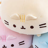Close up of the Round Squisheen plush stacked up in the shape of a triangle, pink and blue at the bottom with the yellow on top. The round squisheen’s ears poke out from a seam, which the head stripe embroidery goes through. Pusheen’s eyes, mouth and whiskers are embroidered in dark brown thread.