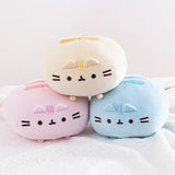 A trio of Round Squisheen plush stacked up in the shape of a triangle, resting on top a fluffy white blanket. All the plush are round, with little stub feet at the bottom, two embroidered stripes on the top, and an embroidered face, whiskers, and head stripes in the middle, with two plush triangle ears sticking out. The pink and blue plush are at the bottom, while the yellow plush sitting on top of them. 
