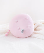 The Pink Round Squisheen resting on her side, showing off her underside. All four nub feet are visible, laid out in a square, an information tag by the bottom right foot. The striped tail pokes downwards.