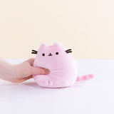 A model’s hand squeezing the Pink Mini Squisheen Plush, demonstrating it’s squishiness