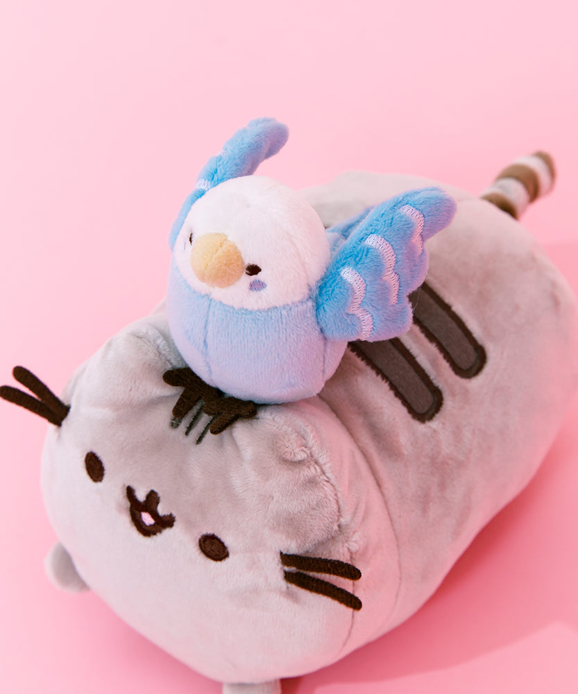 Quarter view closeup of the Bo and Pusheen plush. Bo's eyes, cheeks and features in her wings are embroidered. Bo has a round head, and the white coloring goes down to the top of her wings. Pusheen's face and stripes are embroidered, and her whiskers are two felt stripes on each cheek.