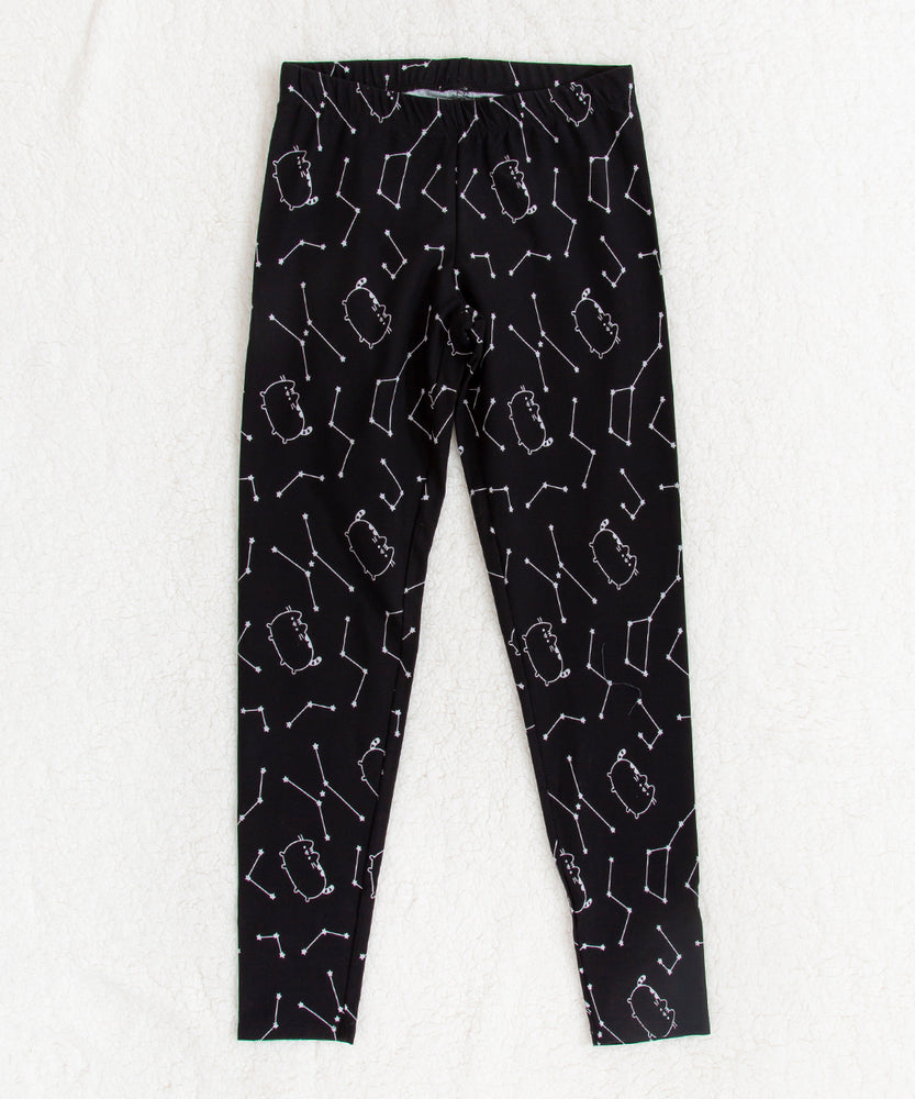 Front view of the Pusheen Celestial Leggings, on top of a white fuzzy blanket.