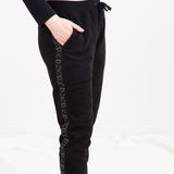 Model wearing the Pusheen Celestial Unisex Jogger, showing the pattern on the side of the jogger with a hand in the jogger's pocket. The jogger has an elastic waistband with a black drawstring tied into a bow. The model is standing in front of a white background.