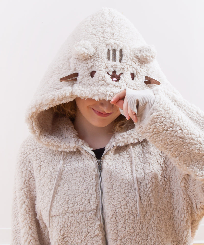 Model sitting on a wooden floor, wearing the Pusheen Character Hoodie with the hood pulled up. The model is smiling while daydreaming. 