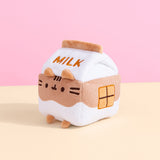 Sitting in front of a pink and yellow background, Chocolate Milk Sips Plush is showing its side profile that showcases an embroidered chocolate square detail.  
