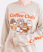   Front and sleeve view of the tan unisex sweatshirt. The arms are folded in to the center of the sweatshirt to reveal the printed sleeve detail. The sleeve features the phrase “Coffee O’ Clock” with Pusheen sitting in a white coffee cup surrounded by two coffee beans.   