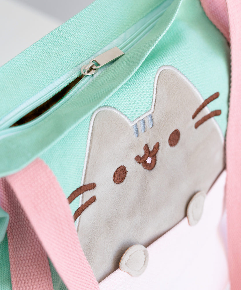 Close-up view of the zipper-closure and Pusheen applique. The tote bag closes shut. The applique of Pusheen is grey velour.  