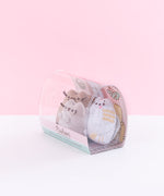 Quarter view of the mini plush in the packaging facing the left in front of a light pink background.