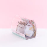 Quarter view of the mini plush in the packaging facing the left in front of a light pink background.