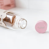 Glass water bottle lies on a white surface showing the inside of the open bottle. The pink top features a Pusheen the Cat logo in silver print.  