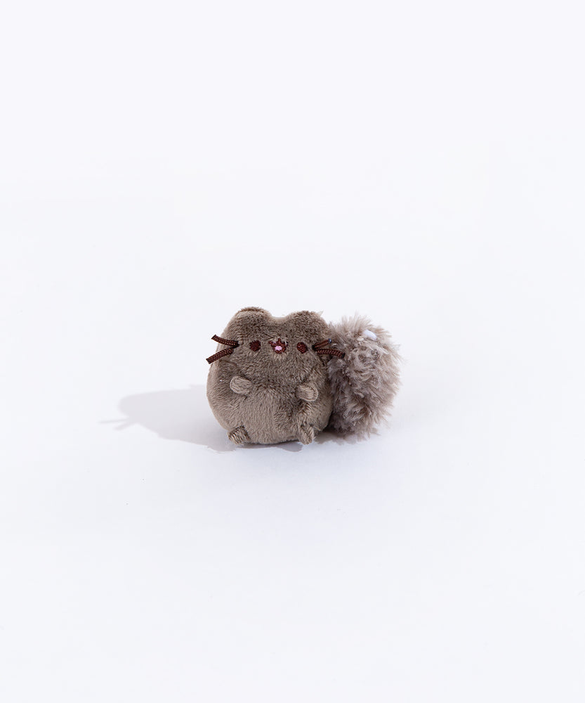 Full view of the mini skunk plush from the collectors set. The skunk resembles Pusheen, but with dark grey fur and a fluffy black tail with a stripe of white felt on top.