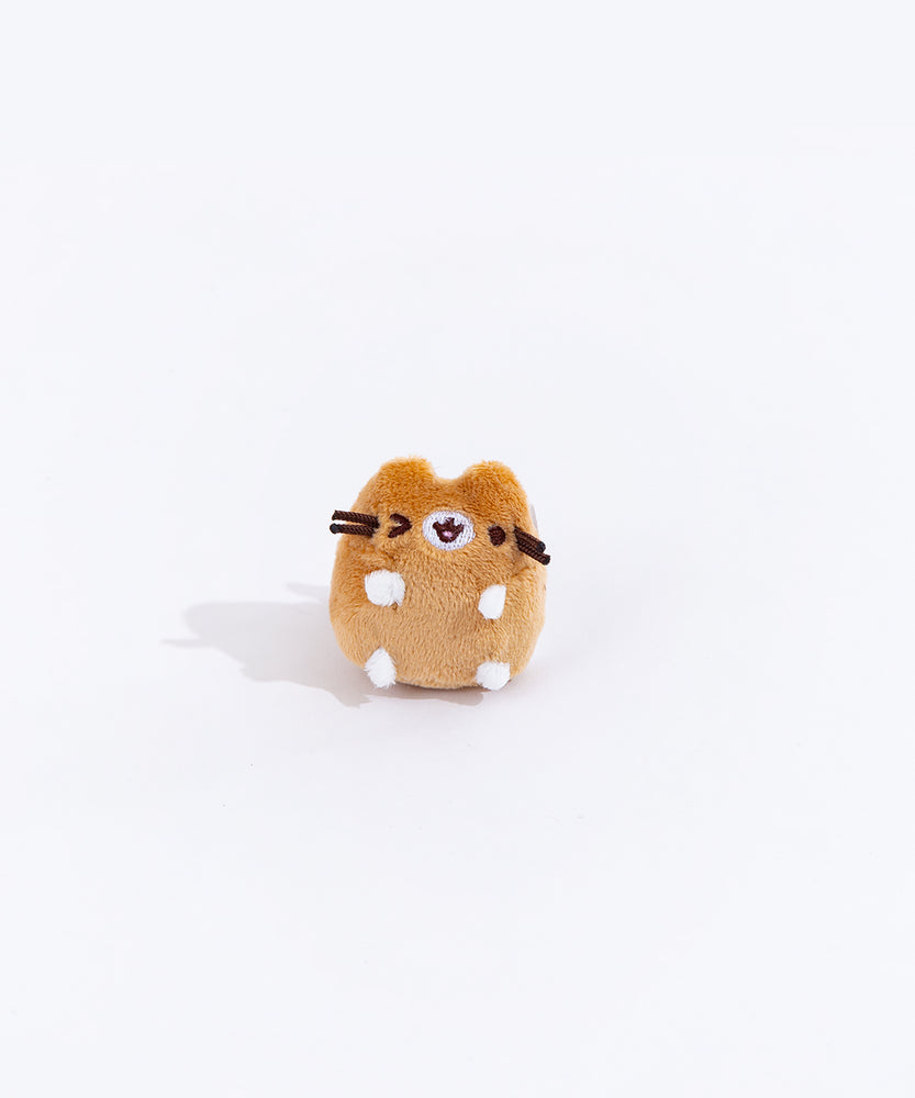 Full view of the mini winking brown cat plush from the collectors set. The cat is a light brown, save for their white paws and a white patch over their mouth. The cat is winking their left eye, and their mouth is slightly open.