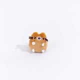 Full view of the mini winking brown cat plush from the collectors set. The cat is a light brown, save for their white paws and a white patch over their mouth. The cat is winking their left eye, and their mouth is slightly open.