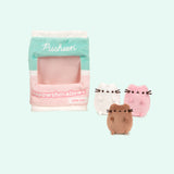 Front view of the miniature brown, white, and pink plush sitting outside of the Meowshmallows bag. The center portion of the bag is see-through.  
